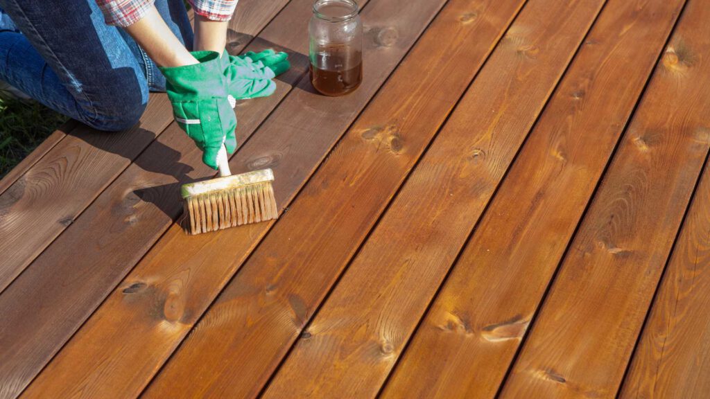 Nahaufnahme eine Holzterrasse, die gerade mit einem Pinsel eingeölt wird